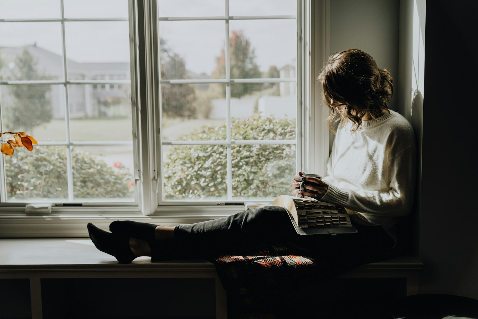 A woman resting on a window seat with a book on a quiet day
