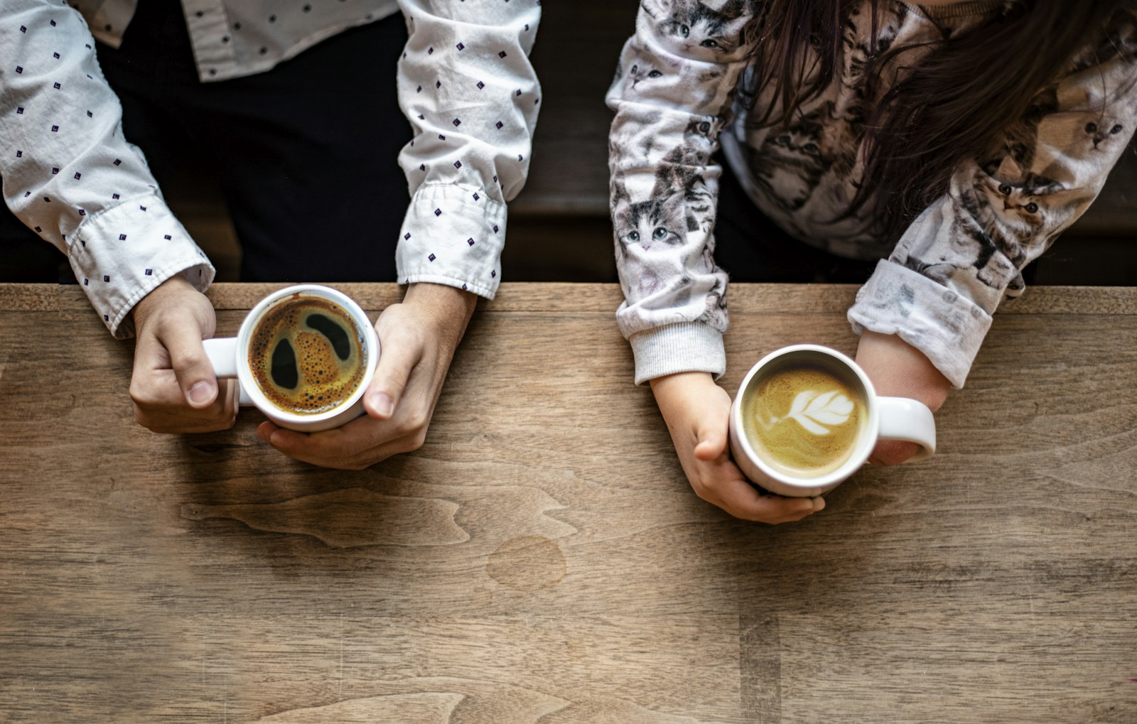 Two people sharing coffee across a wooden table