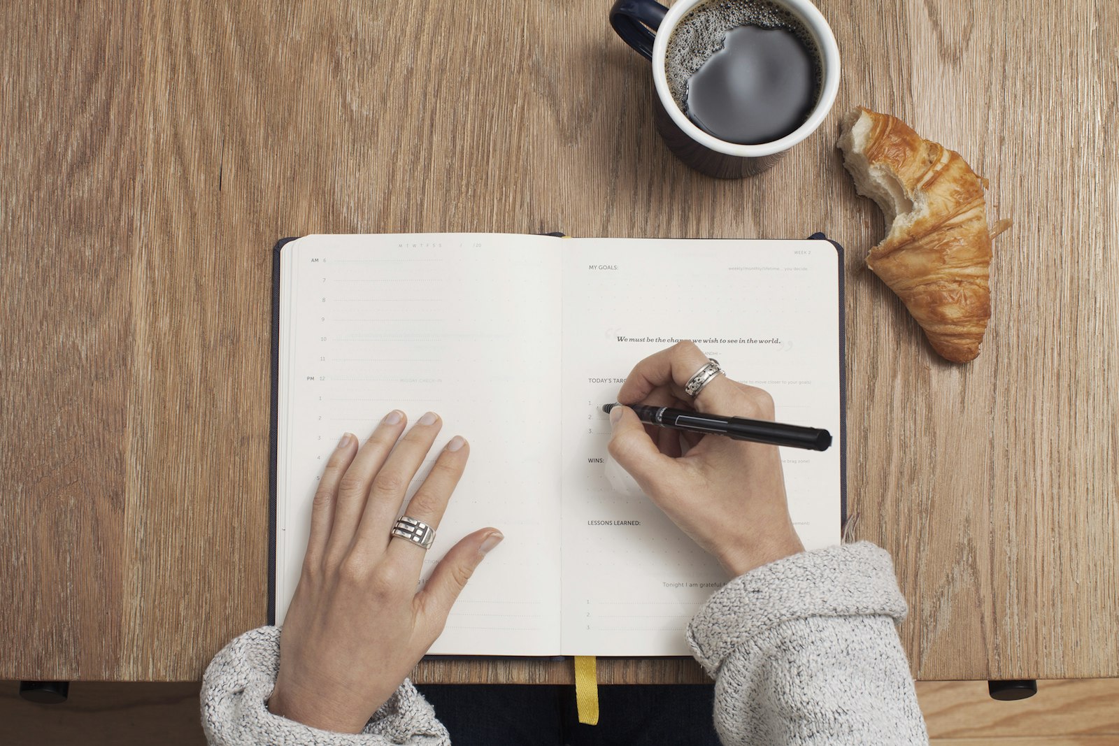 A person writing in a notebook at a wooden table