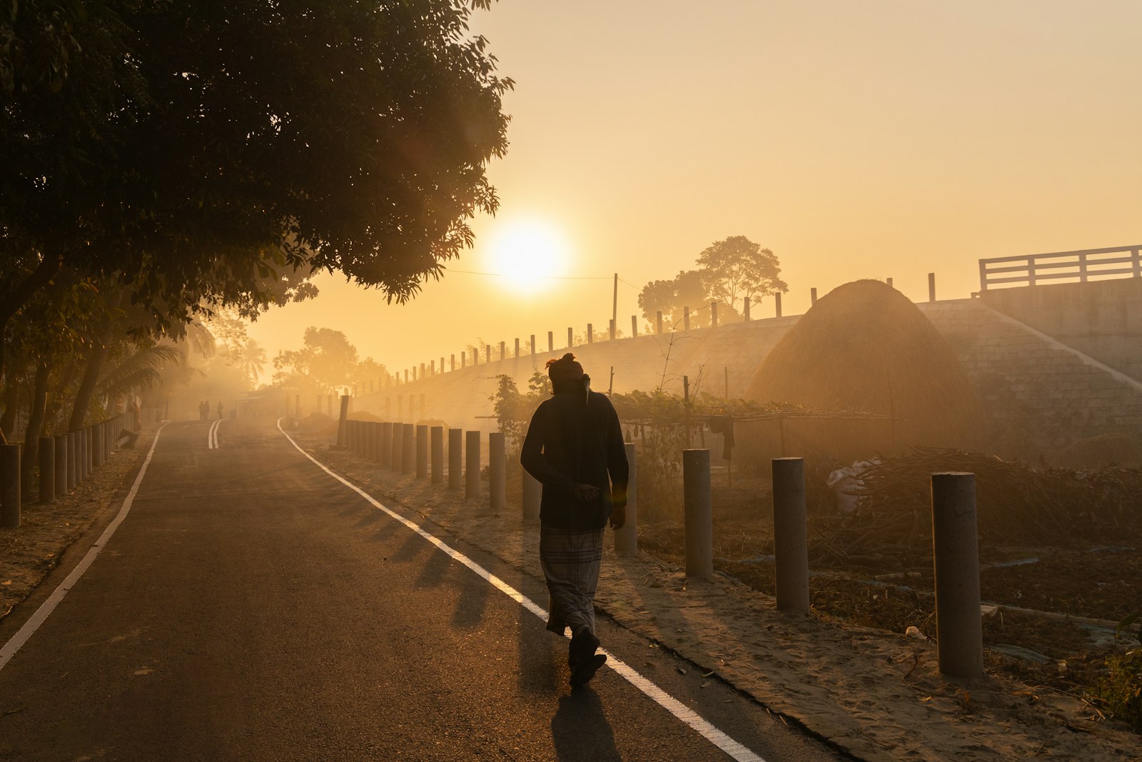 A person walking along a misty road toward a golden sunrise