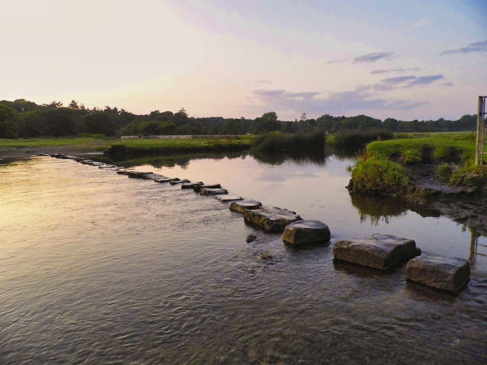 Stepping stones crossing calm water at sunset